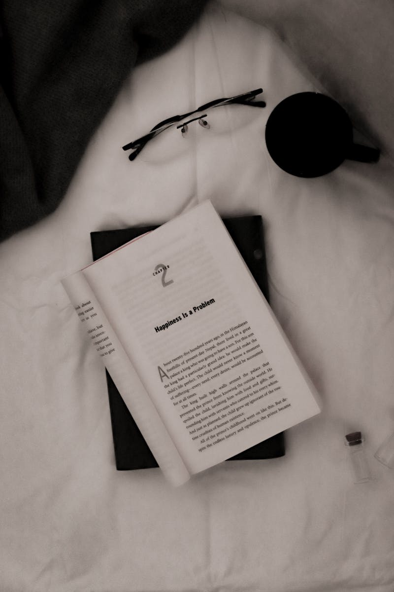 Livro aberto em cima da cama ao lado de óculos e xícara de chá - Metrópoles