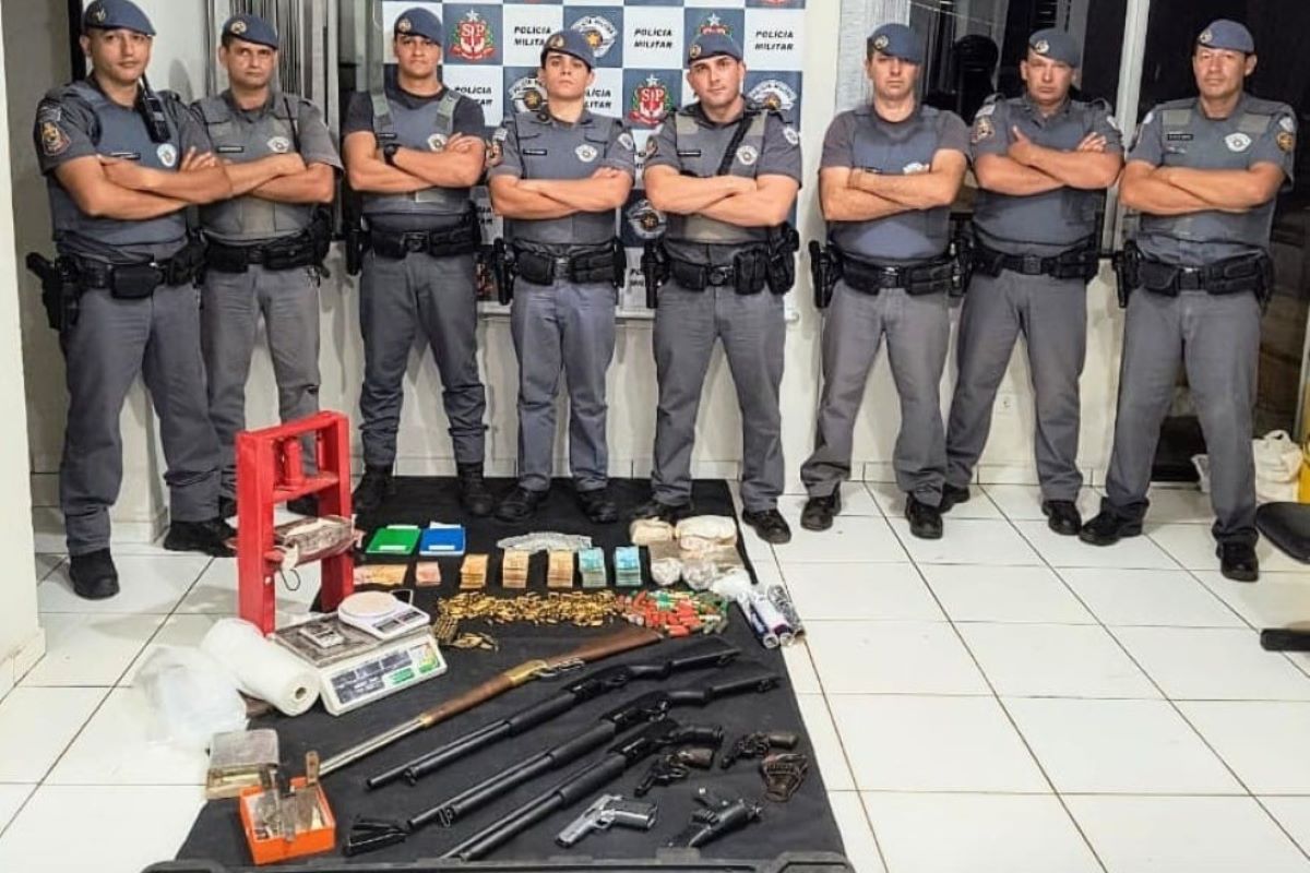 Imagem colorida de policiais posando junto com os materiais apreendidos em operação policial. Metrópoles