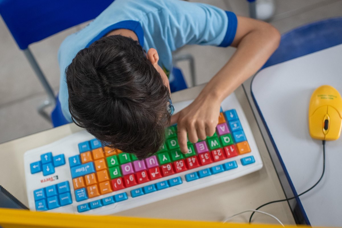 Foto colorida de criança olhando e digitando em um teclado de computador colorido