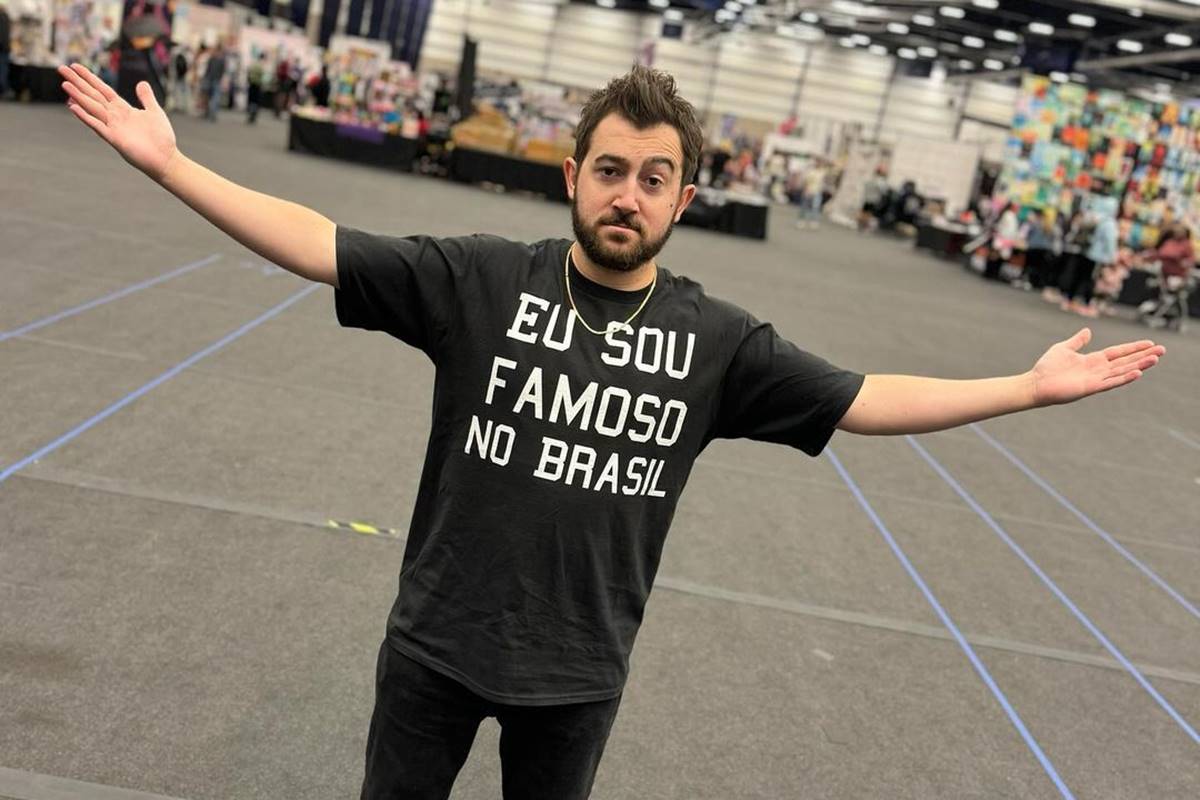 Na foto, homem usa camisa preta com os dizeres "eu sou famoso no Brasil" e está com os braços abertos - Metrópoles