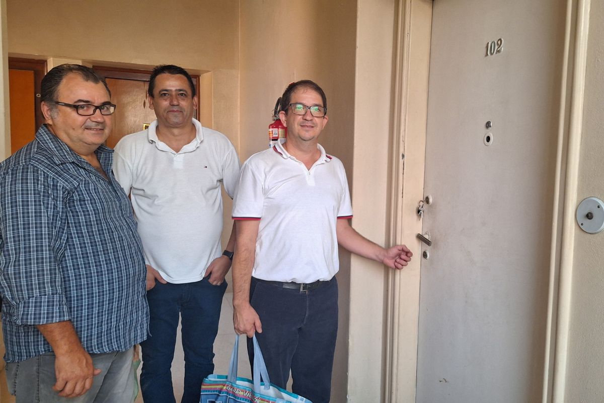 imagem colorida mostra três homens ao lado da porta de um apartamento com o número 102 - metrópoles
