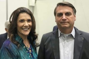 Imagem de mulher branca com cabelo castanho e camisa verde escuro, ao lado de homem com cabelo grisalho e paletó - Metrópoles