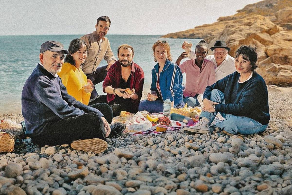 Na imagem colorida, grupo de pessoas está sentado em praia, usando roupas de frio - Metrópoles