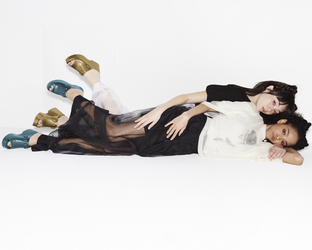 Em fundo branco, uma mulher deitada em cima de outra mulher. Campanha de moda - Metrópoles