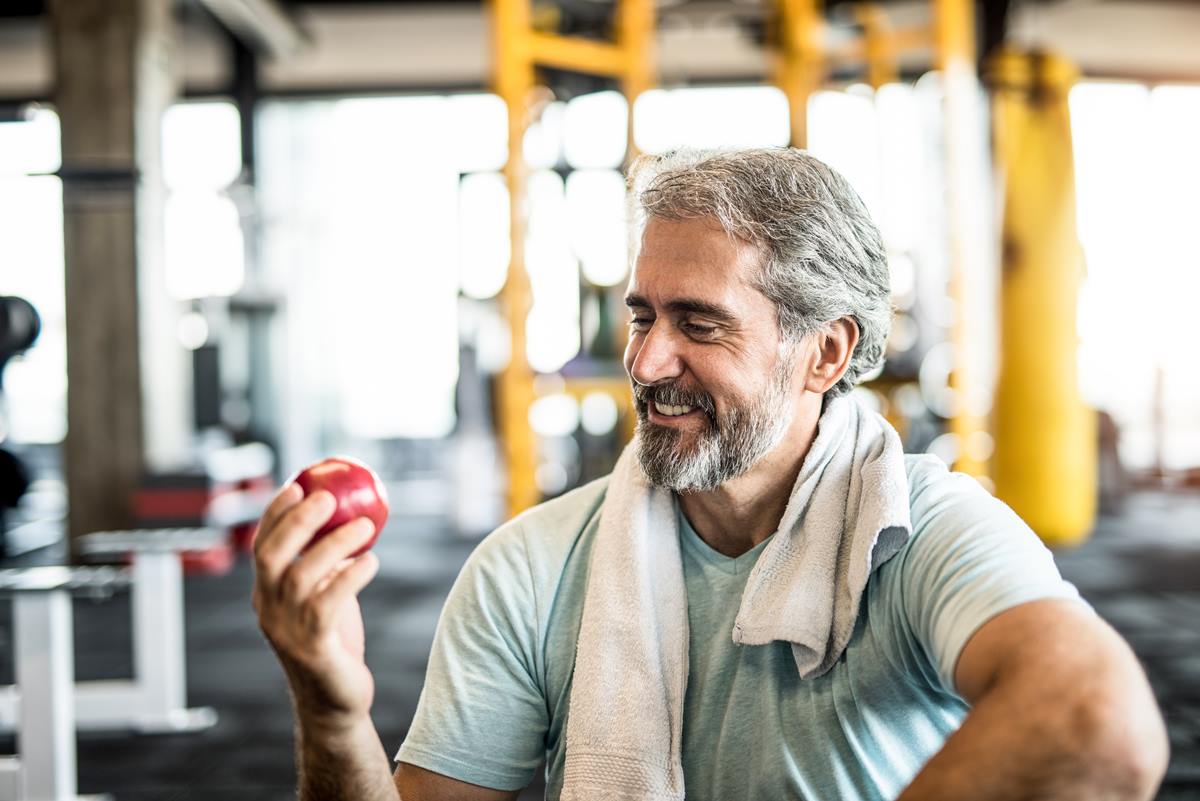 Foto colorida de um homem comendo maça na academia - Metrópoles