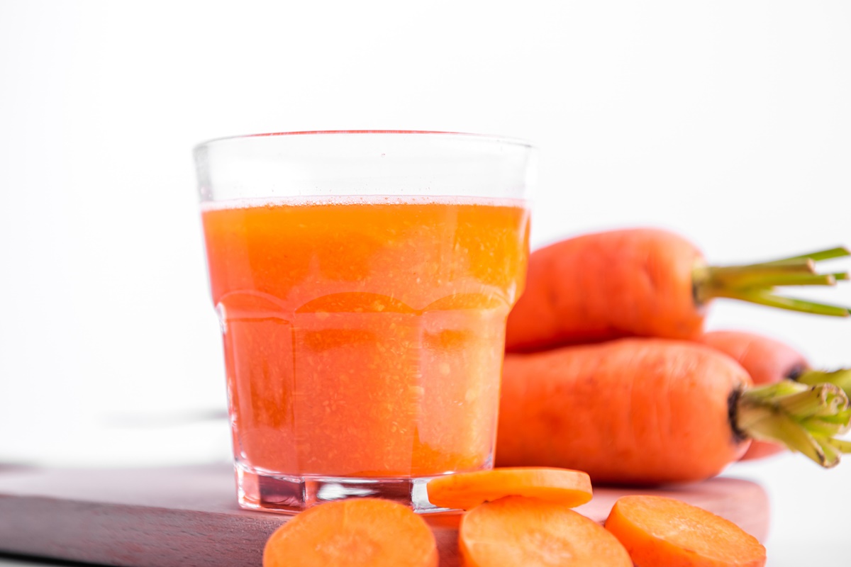 Foto colorida de copo de suco com cenouras cortadas e inteiras ao lado - Metrópoles