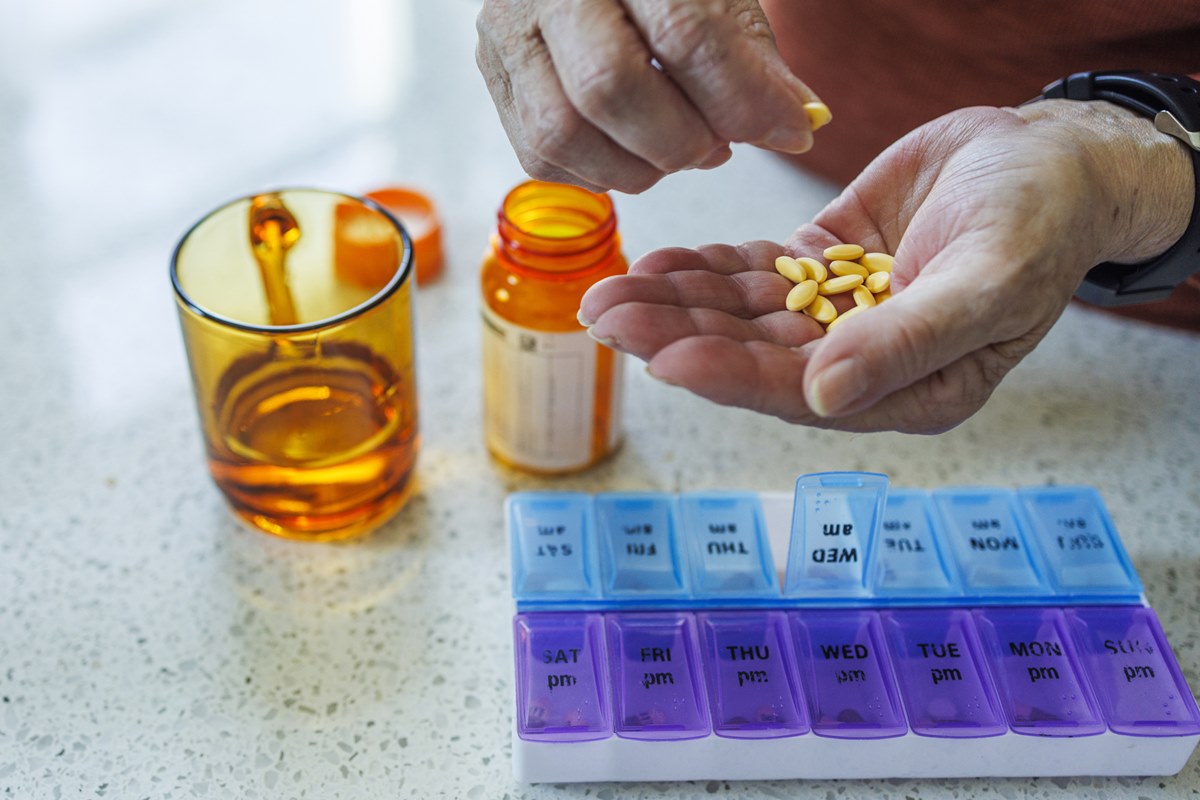 Foto colorida de mão segurando cápsulas de medicamentos e copo de água - Metrópoles