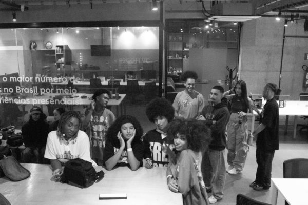 Jovens reunidos em espaço fechado conversam enquanto são fotografados. A imagem está com um filtro em preto e branco.